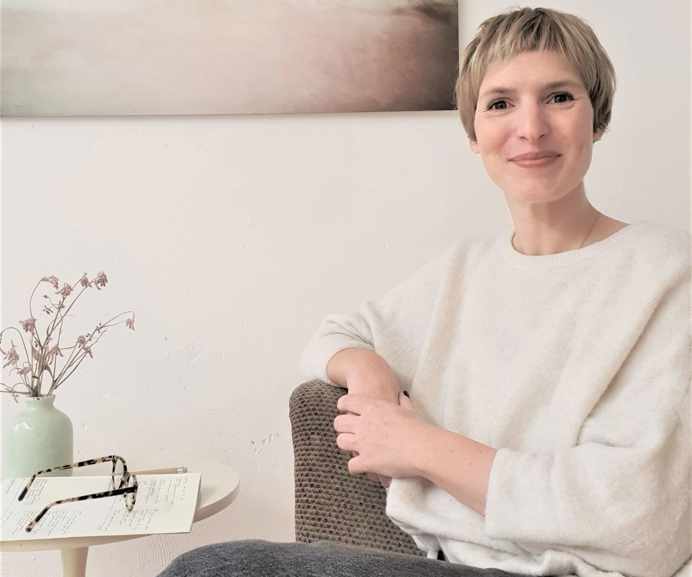 Dies ist ein Foto von Kerstin Dick. Sie sitzt in einer Beratungspraxis und lächelt aufgeschlossen. 